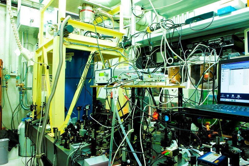 Figure 2: Experimental apparatus for creating excitons at high density and ultra-low temperatures<br>An ultra-low temperature below 0.1 K is maintained in the laboratory, which is equipped with apparatus for observing light and matter, and includes a laser for creating excitons. Because the laser has a heating effect, the temperature will increase if the semiconductor is simply irradiated with the laser. The key to achieving Bose-Einstein condensation of excitons lies in maintaining a low temperature while irradiating the semiconductor with high-energy laser light.<br>Credit: Gonokami, Yumoto, and Yoshioka Laboratory, Graduate School of Science, The University of Tokyo. Figure 2: Experimental apparatus for creating excitons at high density and ultra-low temperatures<br>An ultra-low temperature below 0.1 K is maintained in the laboratory, which is equipped with apparatus for observing light and matter, and includes a laser for creating excitons. Because the laser has a heating effect, the temperature will increase if the semiconductor is simply irradiated with the laser. The key to achieving Bose-Einstein condensation of excitons lies in maintaining a low temperature while irradiating the semiconductor with high-energy laser light.<br>Credit: Gonokami, Yumoto, and Yoshioka Laboratory, Graduate School of Science, The University of Tokyo.
