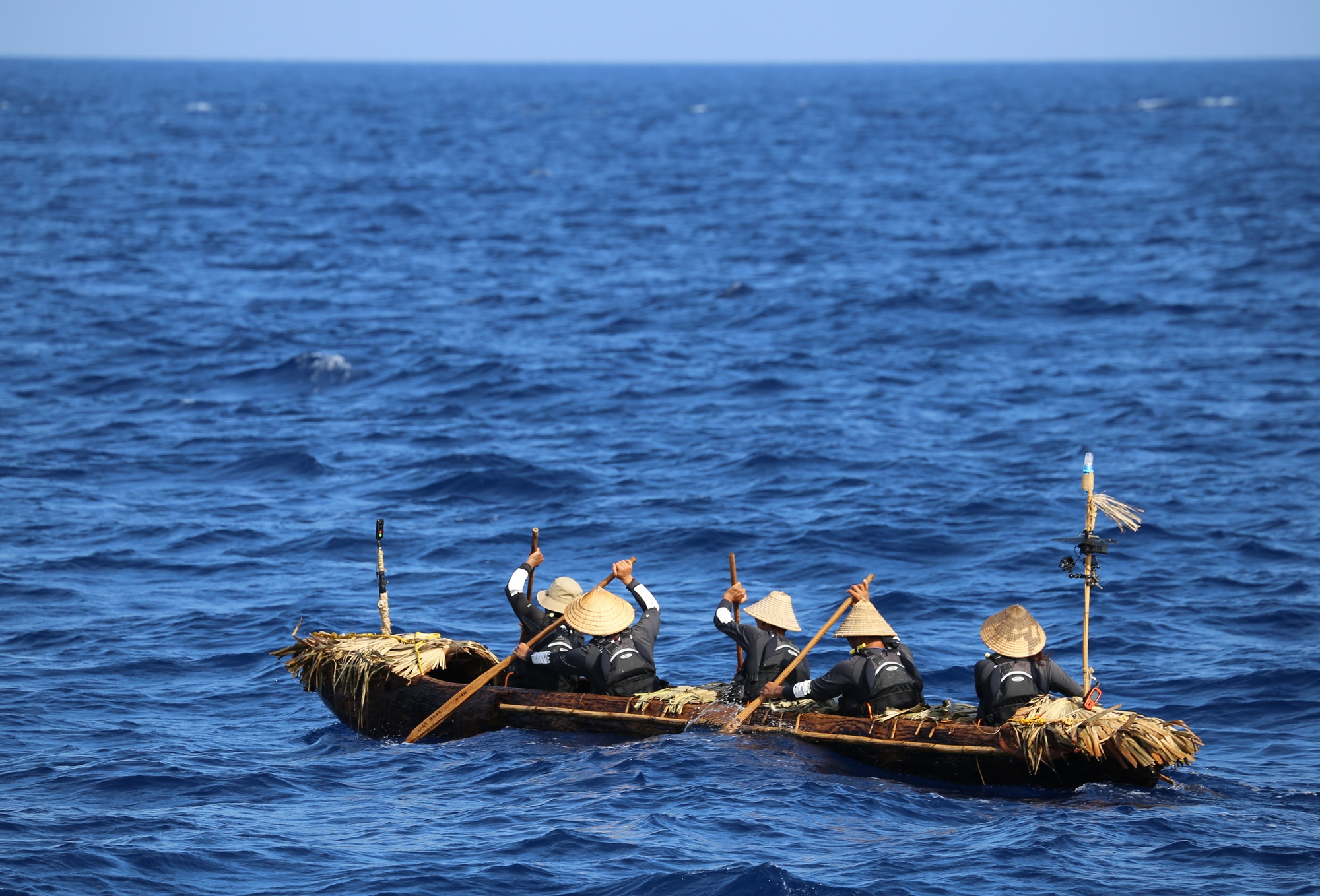 Several people in hats rowing a large canoe on a blue sea