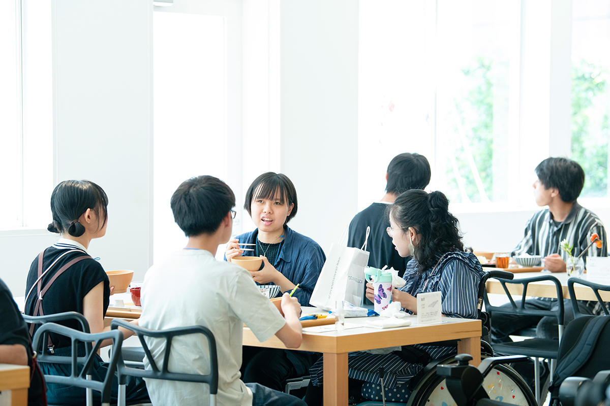 参加者4名がテーブルに座って昼食をとりながら会話をしている様子